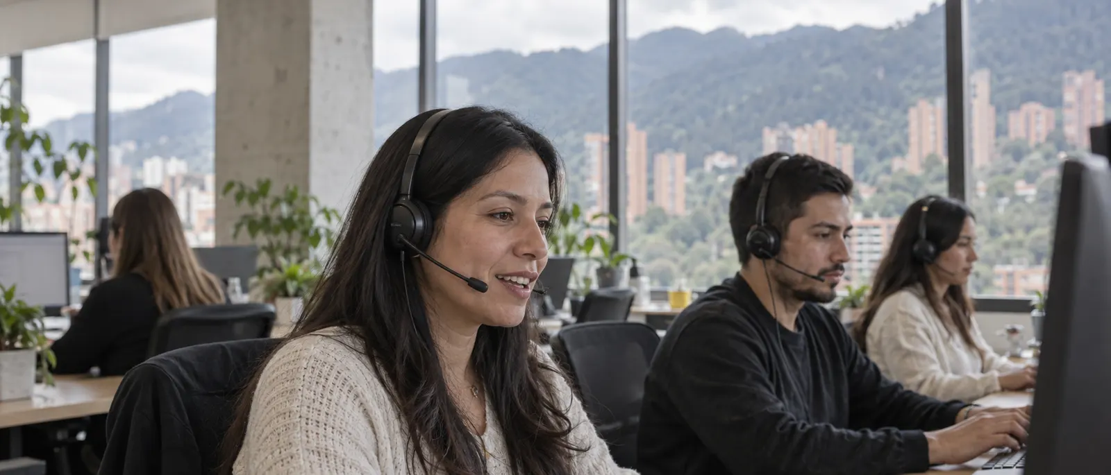 Agents on headsets at the Bogotá studio, with the city and hills through the windows